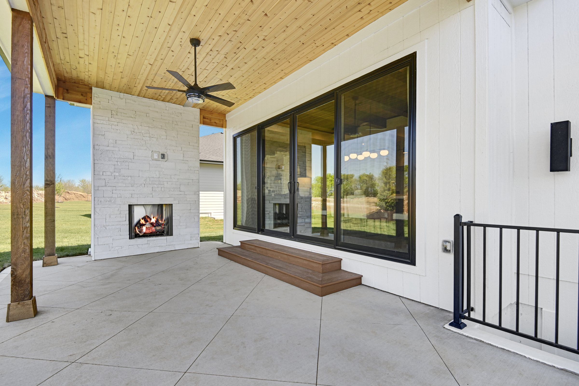 Covered patio with a white stone outdoor fireplace and cedar ceiling at a JFE Construction home