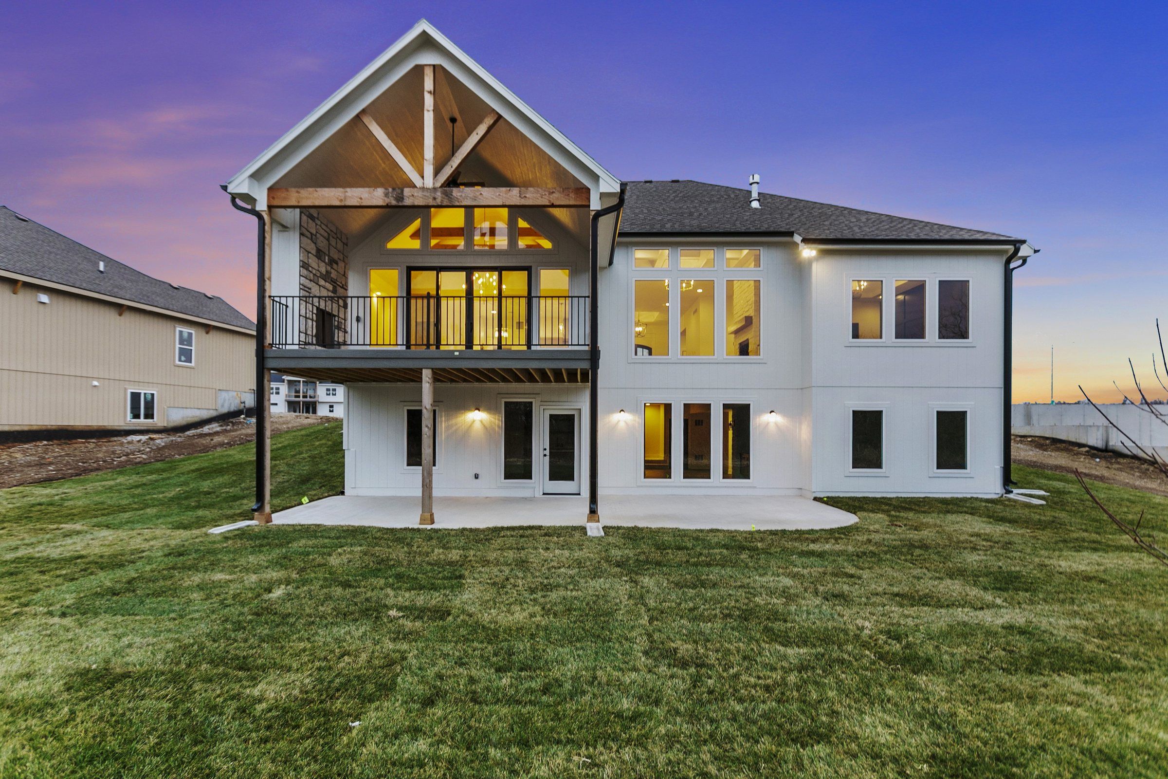 Rear of a JFE Construction home at twilight with a lit covered deck over a walkout lower level